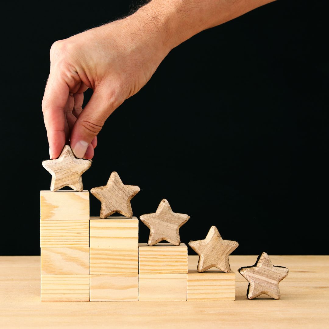 Five wooden stars on top of wooden blocks, with a hand grabbing one of them.